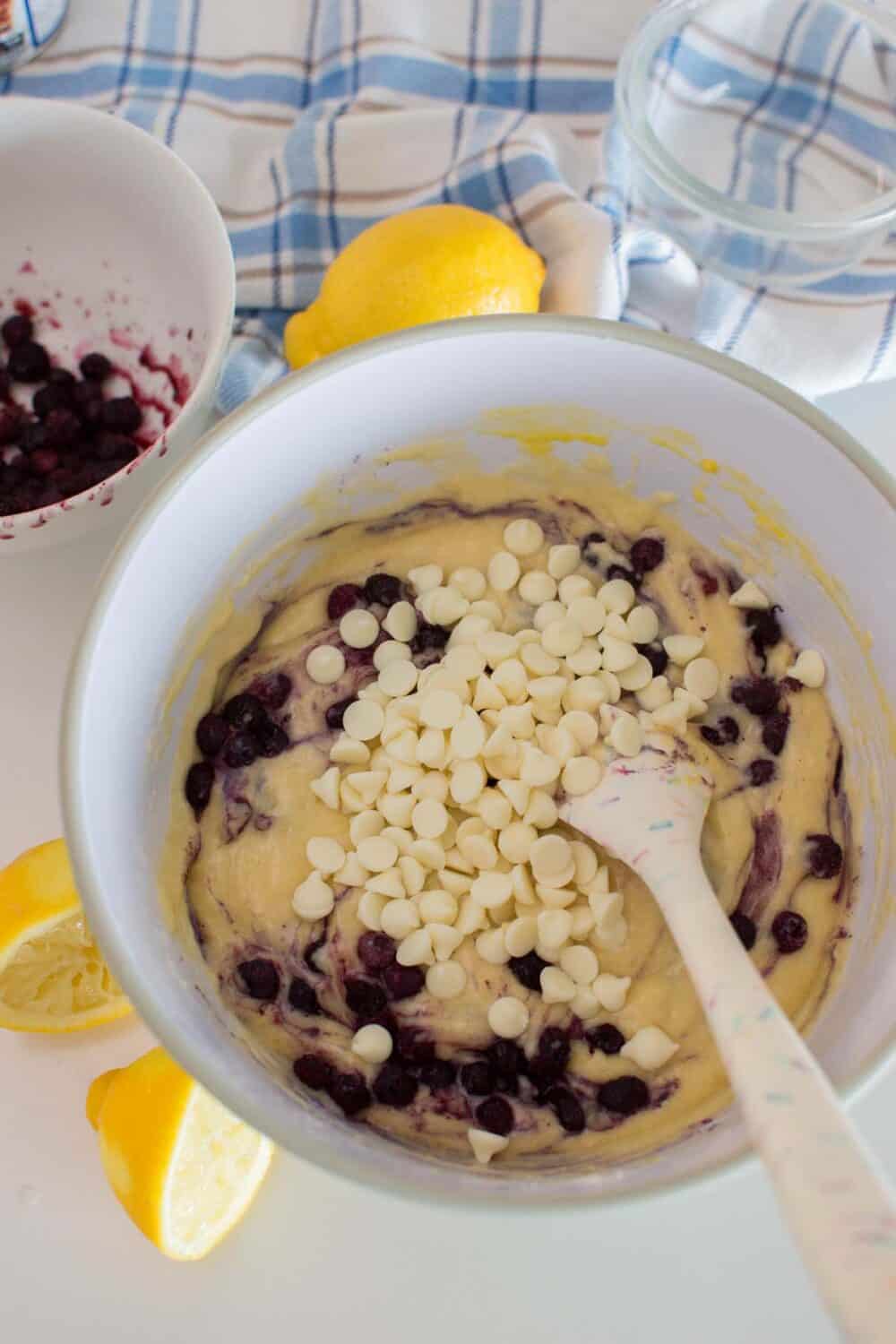 Overhead shot of white chocolate chips being folded into lemon and blueberry muffin batter
