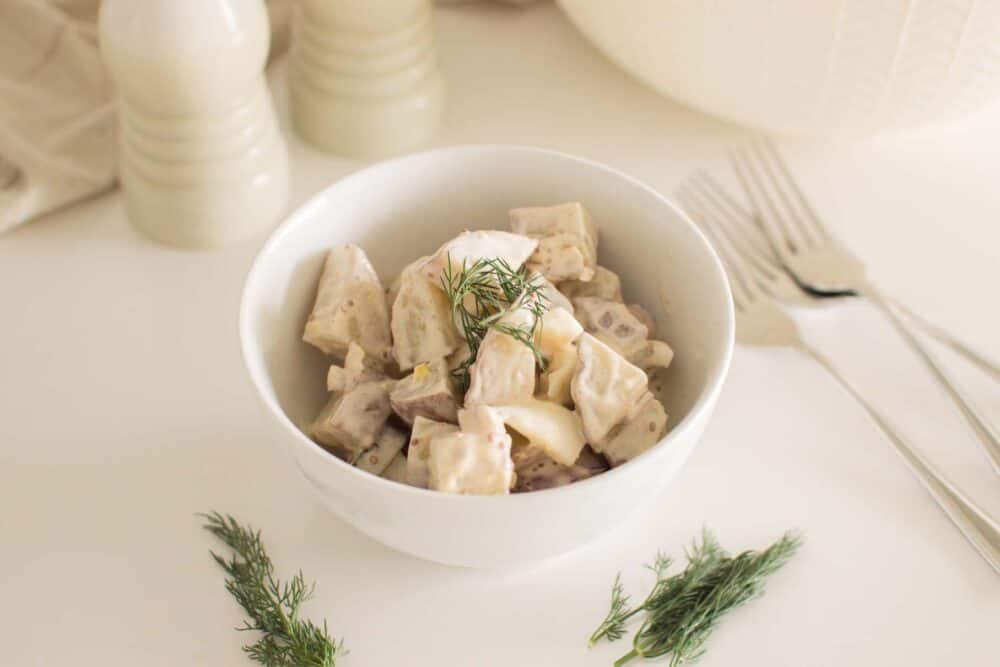 Bowl of loaded dill pickle potato salad garnished with fresh dill
