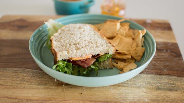 Fresh ham and lettuce sandwich with chips on a teal plate, cozy snack setup.