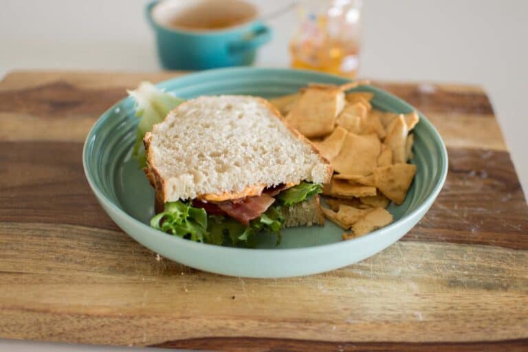 Fresh ham and lettuce sandwich with chips on a teal plate, cozy snack setup.
