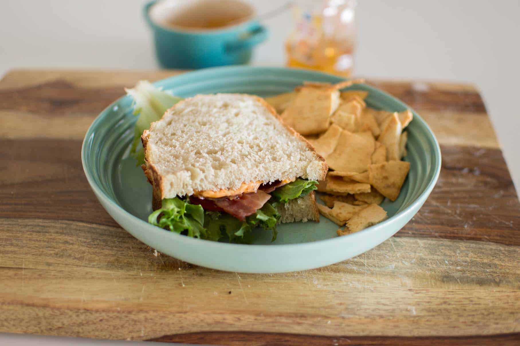 Fresh ham and lettuce sandwich with chips on a teal plate, cozy snack setup.