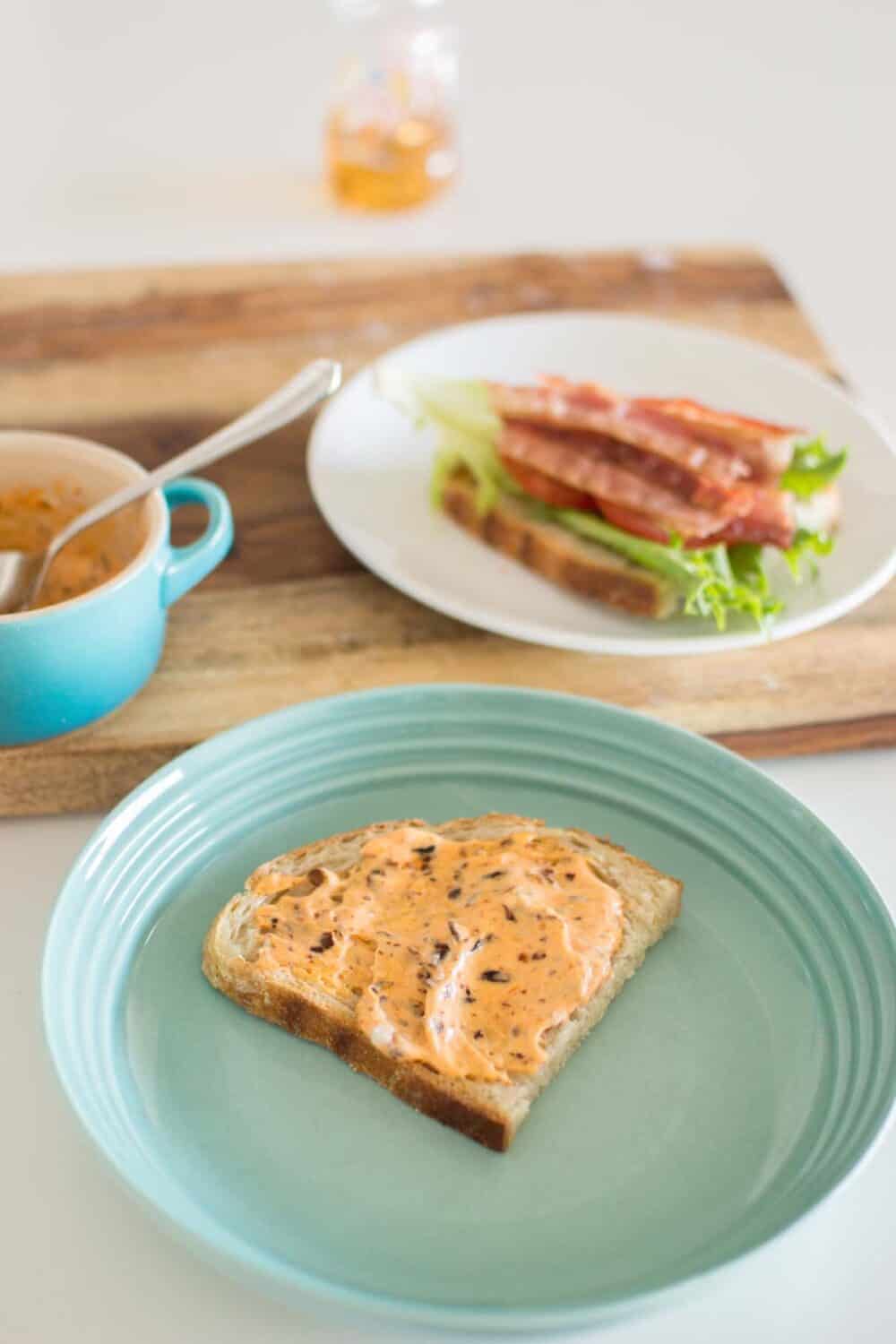 Mayo mixture being spread on toasted bread for BLT sandwich