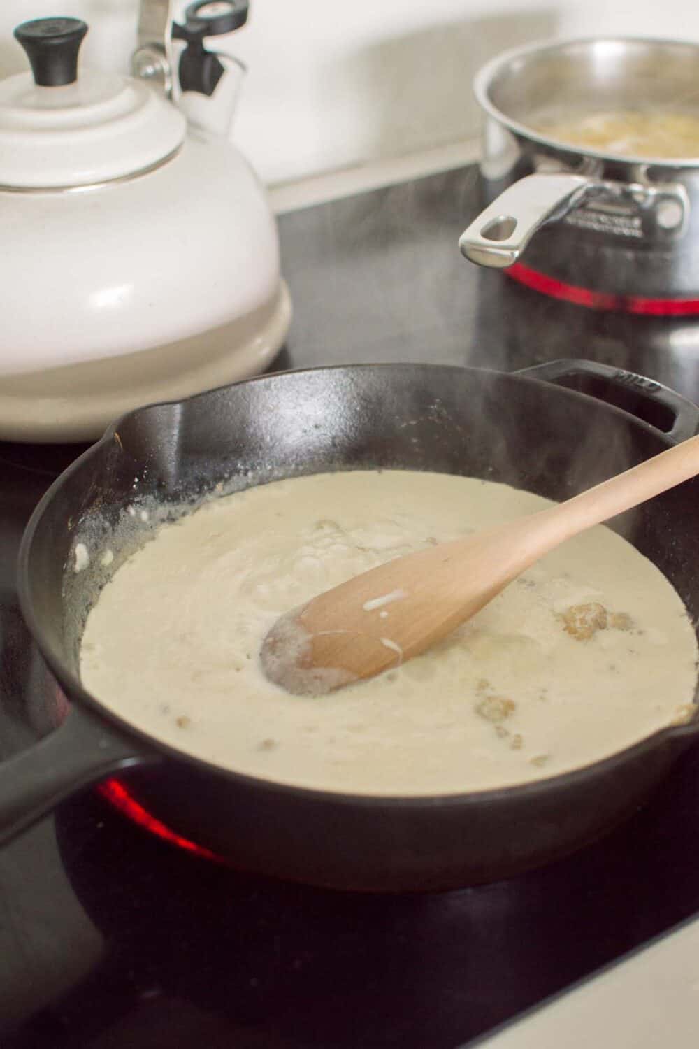 Creamy parmesan sauce being stirred in a skillet for spinach orzo