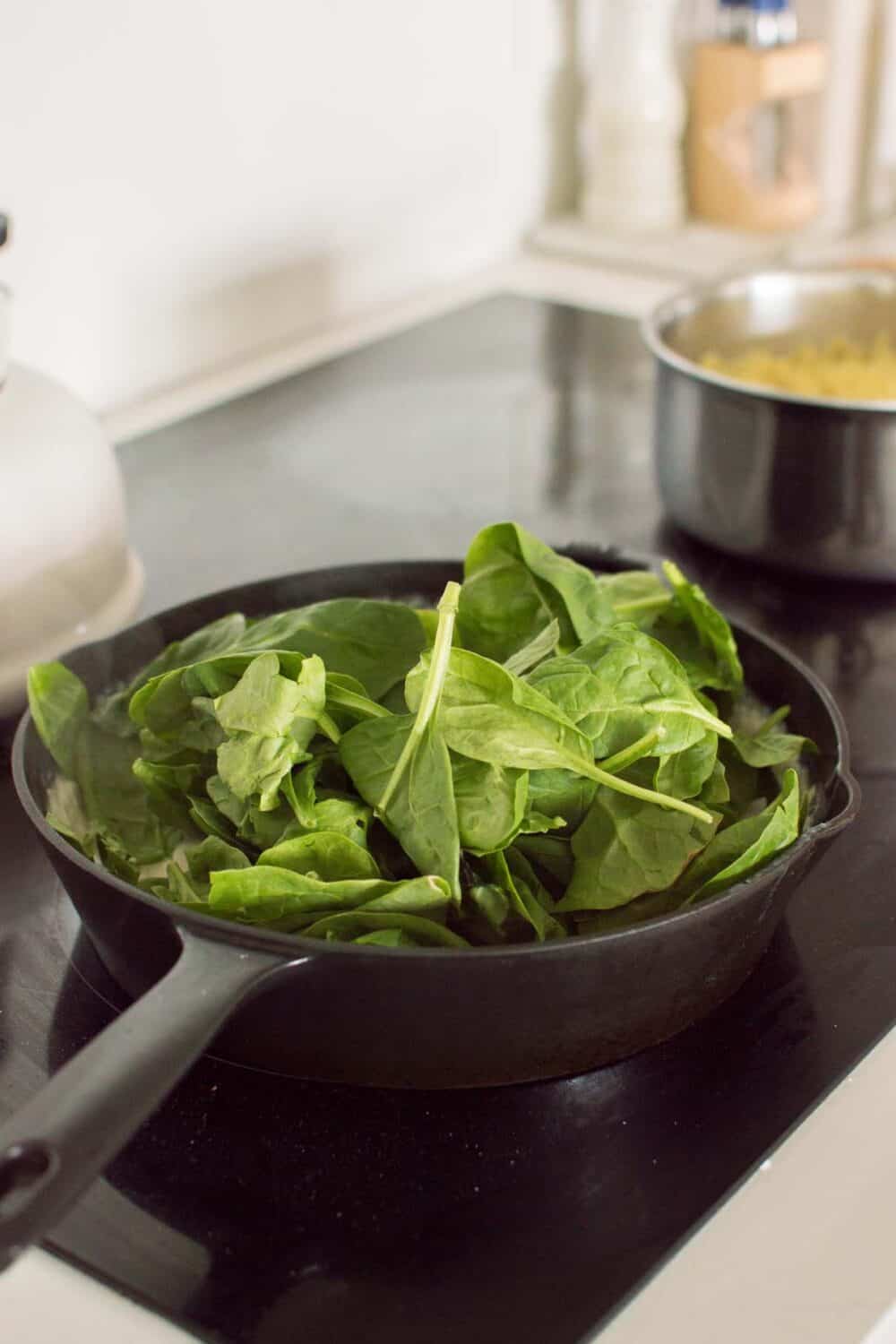 Fresh spinach being added to creamy parmesan sauce in a skillet