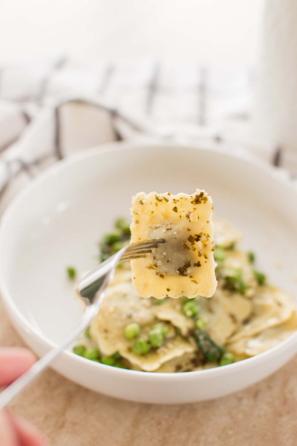Fork lifting a piece of cheese ravioli from a bowl of creamy pesto pasta
