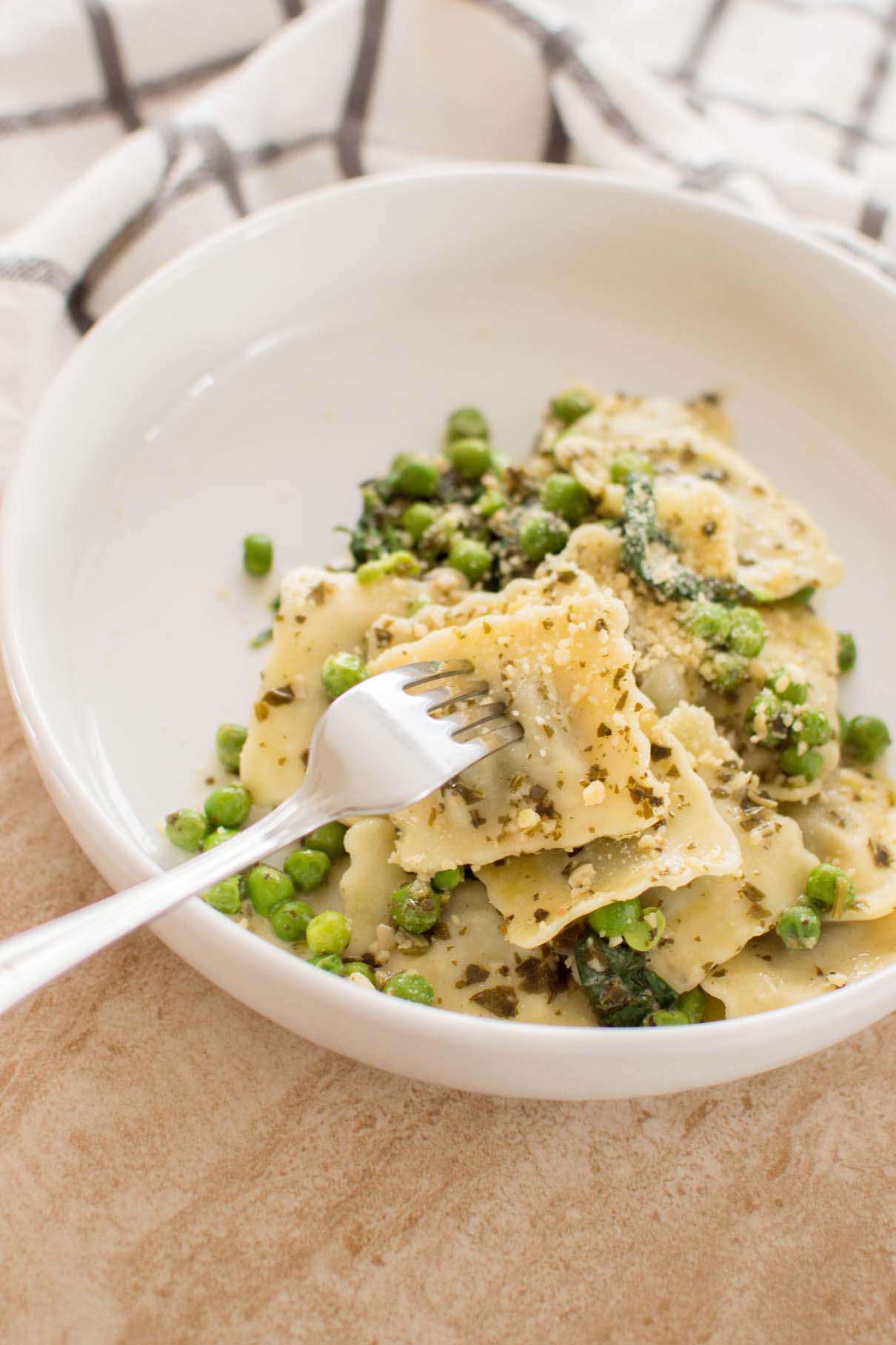 Fork lifting a piece of cheese ravioli from a bowl of creamy pesto pasta