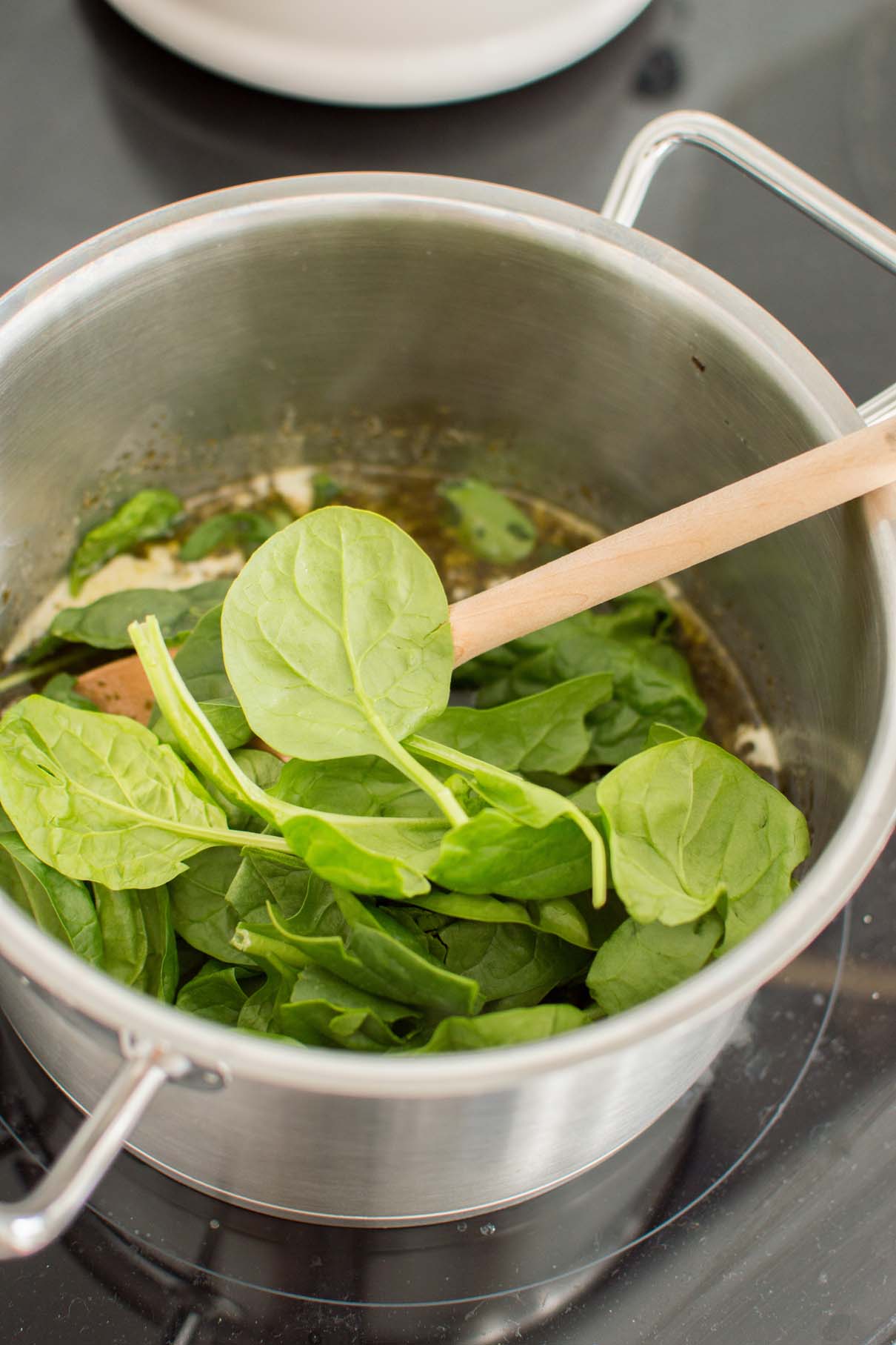 Fresh baby spinach added to a saucepan while preparing creamy pesto ravioli